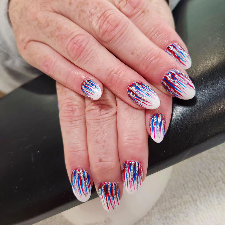 white round nails with red, blue, and silver glitter streaks raining down from the cuticles like fireworks