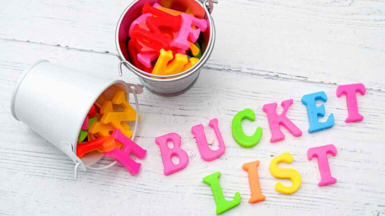 two small metal buckets sitting on a white wooden table, one knocked over with magnetic letters spilling out spelling "bucket list"