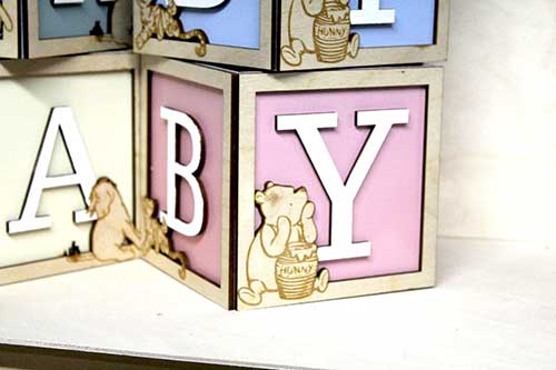 a pink wooden baby block featuring laser-cut classic Pooh characters