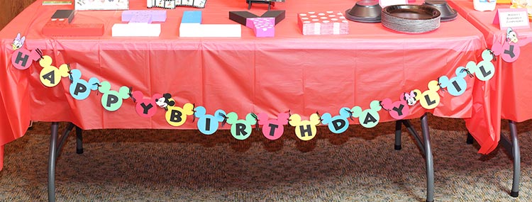 a birthday party table setup with a large banner made of Mickey head silhouettes that reads "Happy Birthday Lily"