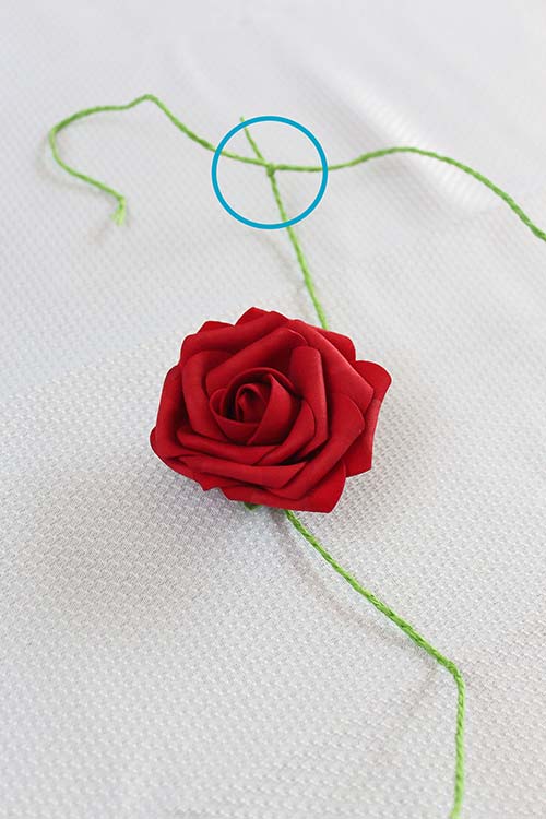 a fake red rose attached to a vine that is tied to a garland