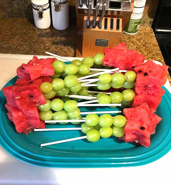 a tray full of fruit skewers that resemble fairy wands with grape handles and watermelon star cutouts on the ends
