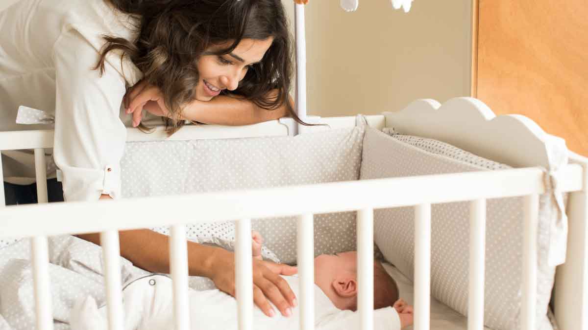 a mother leaning over a crib and patting her baby