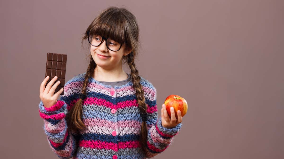 a young girl in braids holding up a bar of chocolate in one hand and an orange in the other