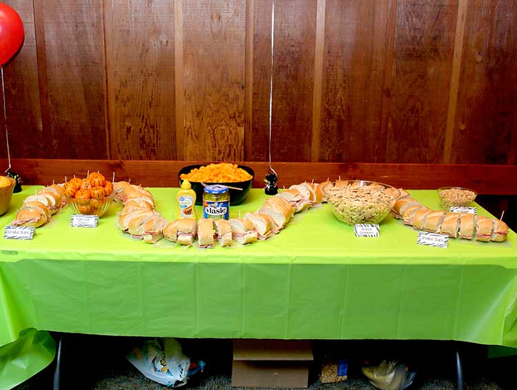 a party food table with an extremely long, sliced-up sub sandwich snaking around the other food items