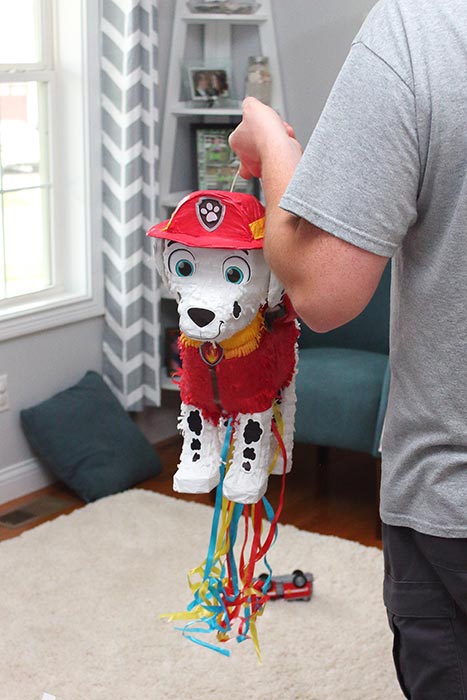 a man holding up a pinata made to look like Marshall from Paw Patrol