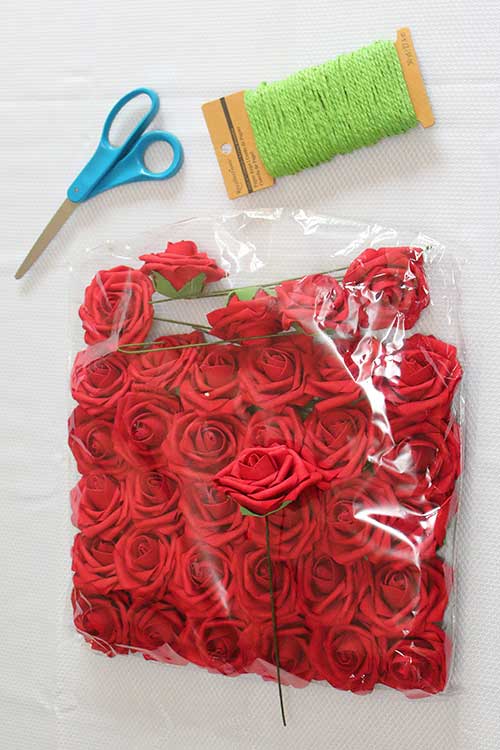 scissors, green paper rope, and fake red roses lying on a white table