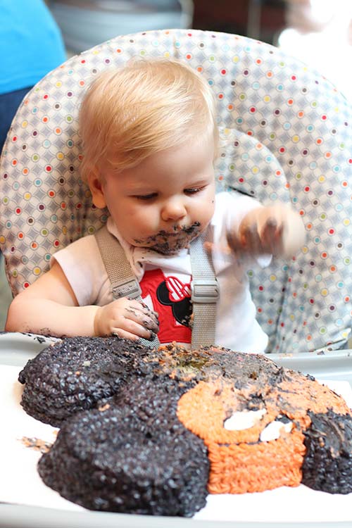 a one-year-old girl making a mess with her Mickey Mouse smash cake on her first birthday