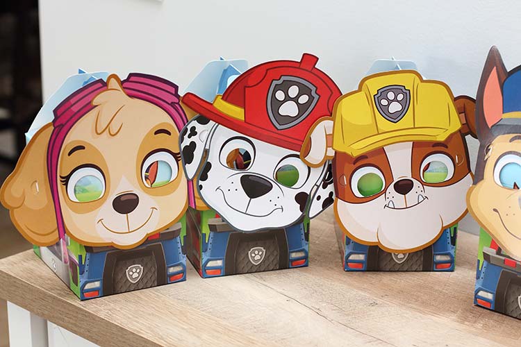three Paw Patrol-branded party favor boxes with paper masks of Skye, Marshall, and Rubble attached to them