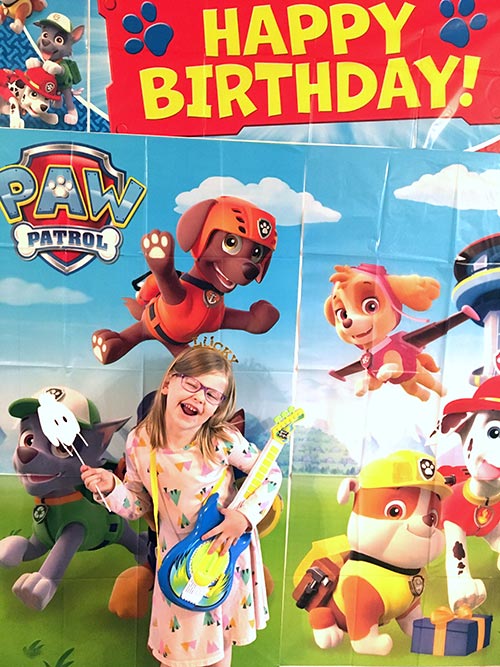 a little girl holding an electric guitar standing in front of a Paw Patrol photo backdrop