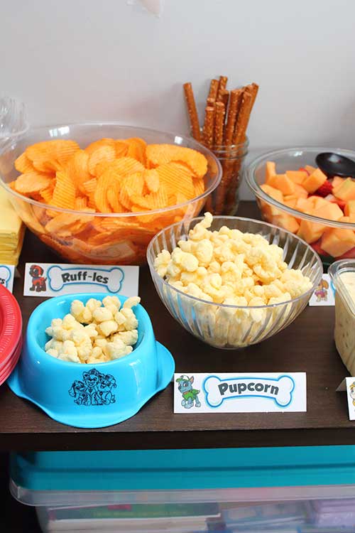 a blue Paw Patrol-branded dog food bowl full of white cheddar puffcorn and a label that says "Pupcorn"
