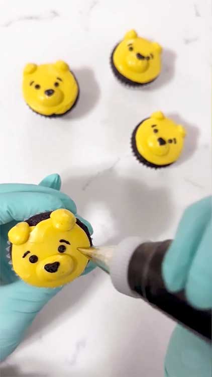 a baker decorating cupcakes to look like Pooh's face