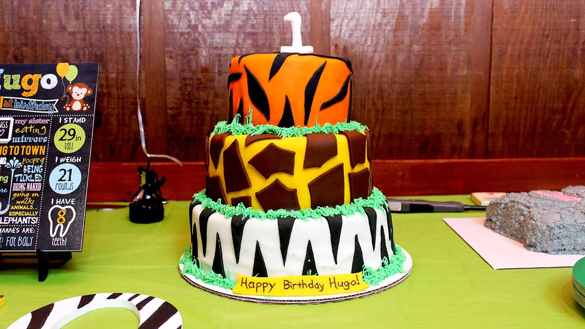 a three-tier safari jungle animal birthday cake, each layer a different animal print: tiger stripes, giraffe spots, and zebra stripes