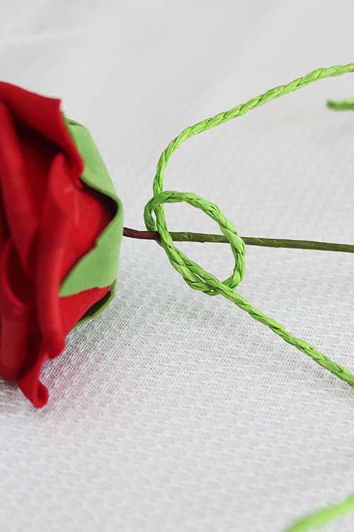 a loose overhand knot in green paper rope wrapped around a silk rose stem