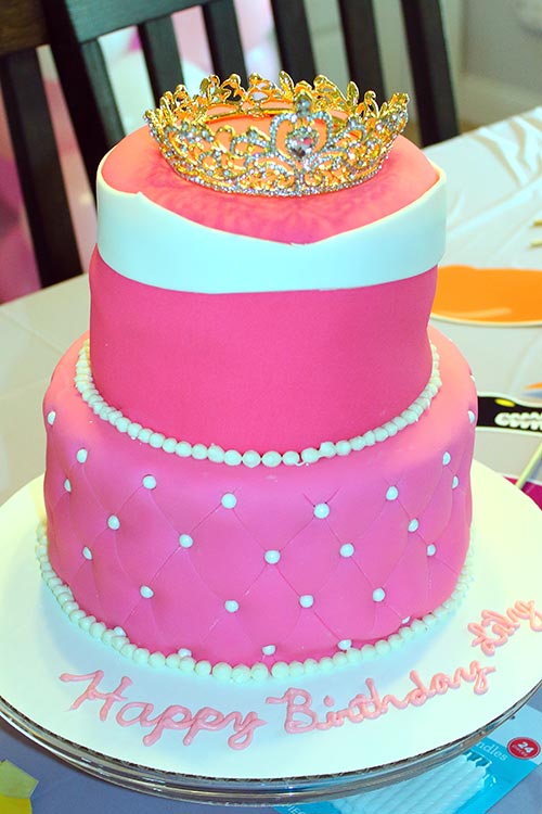 a two-tier fondant cake made to resemble Princess Aurora's pink dress from Sleeping Beauty, with a gold princess crown resting on the top layer