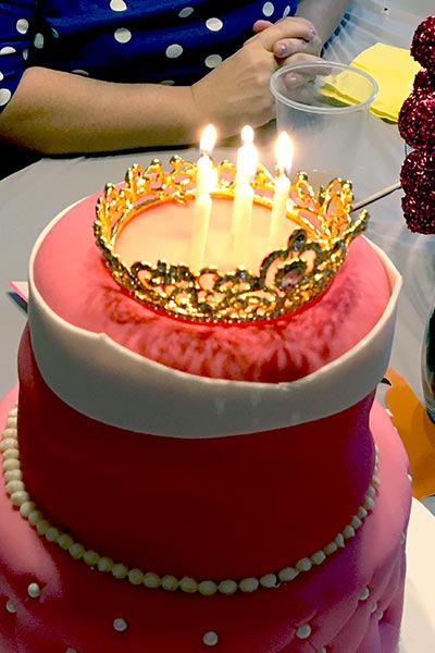 lit birthday candles placed inside a gold crown on a pink birthday cake