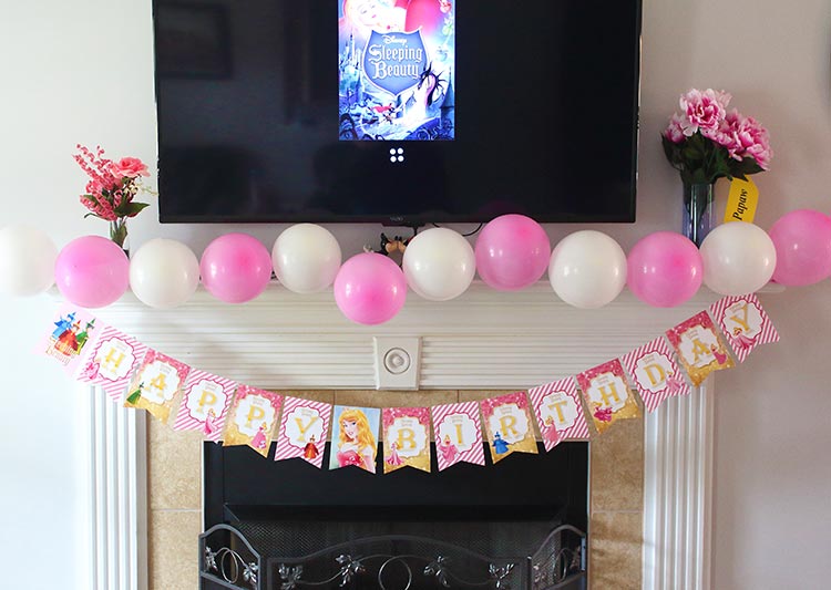 a fireplace decorated in pink and white balloons and a Sleeping Beauty-themed happy birthday banner