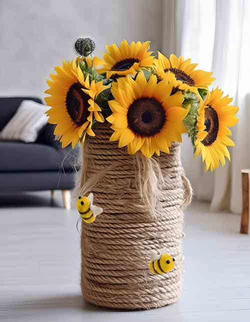 a vase wrapped in craft rope with small felt bees attached to it; sunflowers stick out from the top of the vase