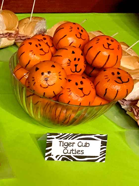orange cuties in a bowl with tiger faces and stripes drawn on them in black marker, with a food card labeled 