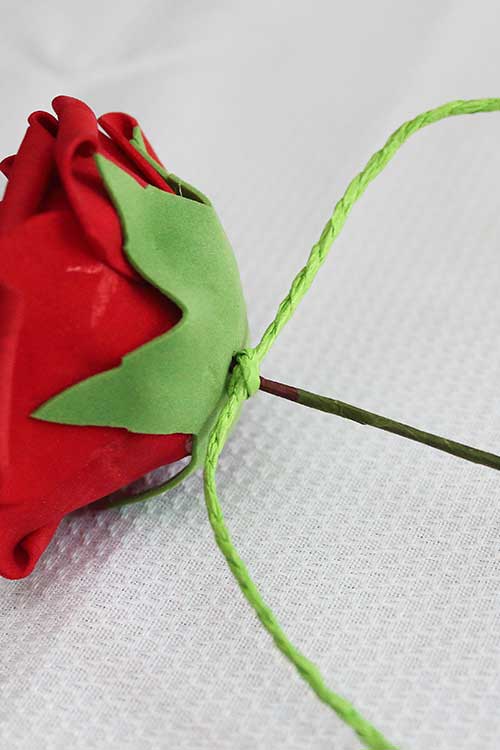 an overhand knot in green paper rope pulled tight against a silk rose bloom