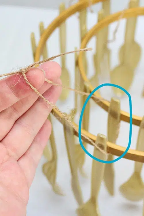 hand holding up a knot of twine attaching two chandelier tiers