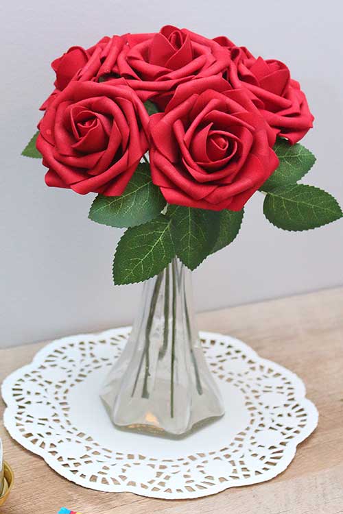 a bouquet of gorgeous red silk roses in a small clear vase resting on a white doily