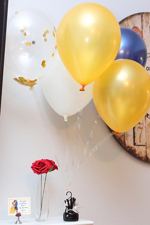 navy, gold, and white balloons floating above a small vase of red roses