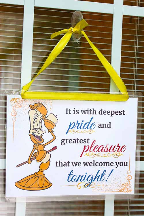 a homemade door sign featuring Lumiere that reads "It is with deepest pride and greatest pleasure that we welcome you tonight!"