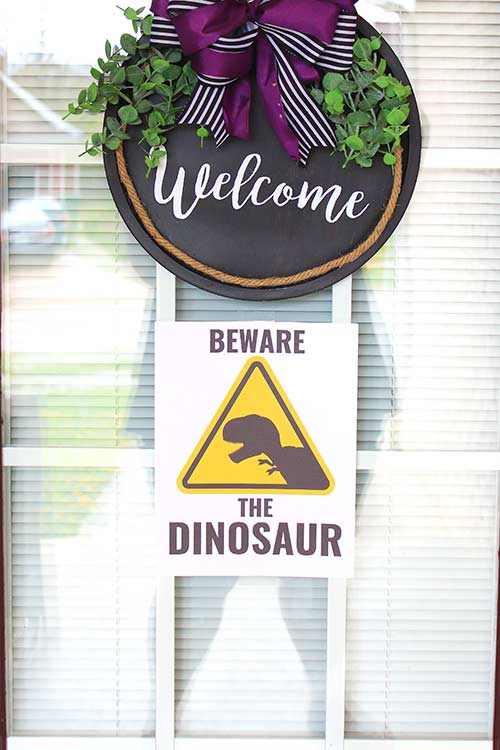 a welcome door sign with a caution sign below that reads "Beware the DINOSAUR"