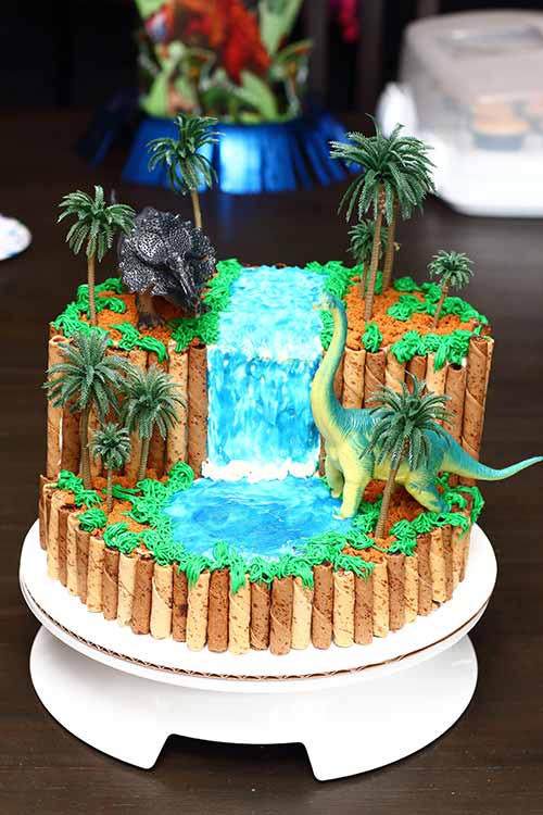 a cake made to look like a realistic waterfall with dinosaurs and palm trees