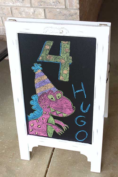 a chalkboard with a pink T-rex drawn in chalk, the number 4, and the name "Hugo"