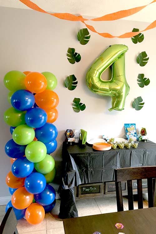 a balloon column of orange, blue, and green balloons, a large green 4 balloon, and large jungle leaves surrounding it on the wall