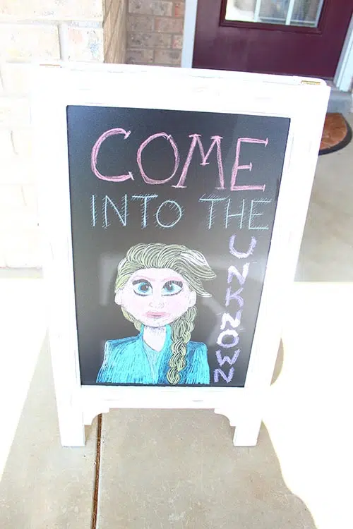 a chalkboard sign that says "Come Into the Unknown" with a drawing of Elsa from Frozen at the bottom