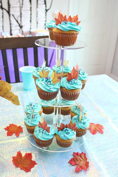 a cupcake stand full of teal-frosted cupcakes with sprinkles and edible fall leaves on top