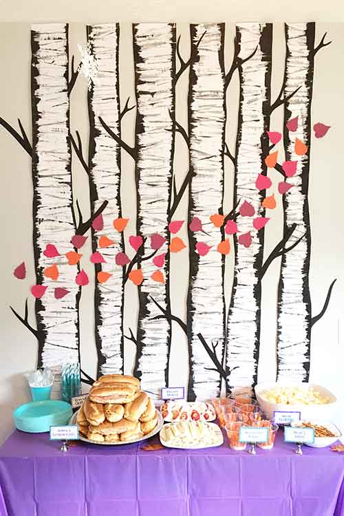 DIY paper birch trees covering a wall with cardstock pink and orange leaves appearing to blow around them