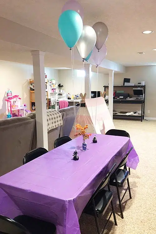 a folding table set up in a basement with a purple table cover, fall leaf centerpiece and balloons