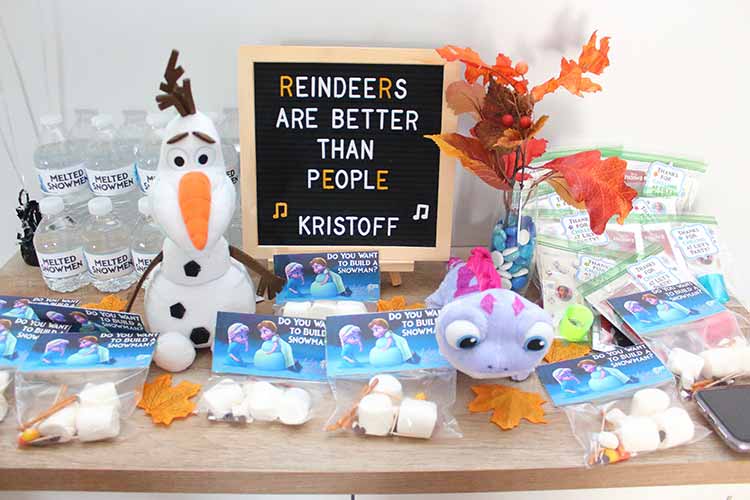 a cabinet covered in Olaf water bottles, an Olaf plushie, snowman-building kits, Bruni from Frozen 2, fall leaf decor, and party favor bags