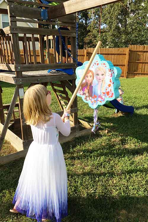 a little girl hitting a Frozen 2 pinata with a stick