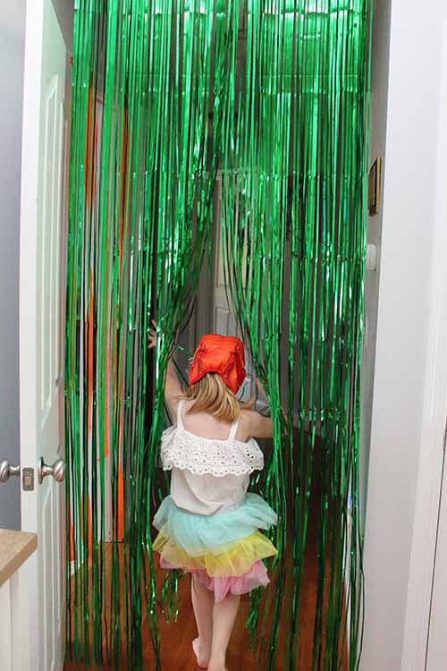a girl wearing a dinosaur head walking through a green party curtain