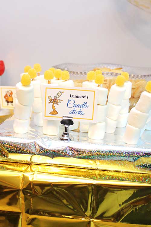 skewers of jumbo marshmallows with yellow gumdrops on top that resemble candles with a food card labeled "Lumiere's Candlesticks" featuring the named character