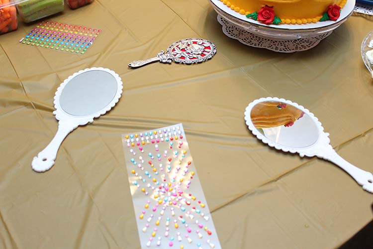 a table covered in gold with several white handheld mirrors and sheets of gem stickers for decorating them