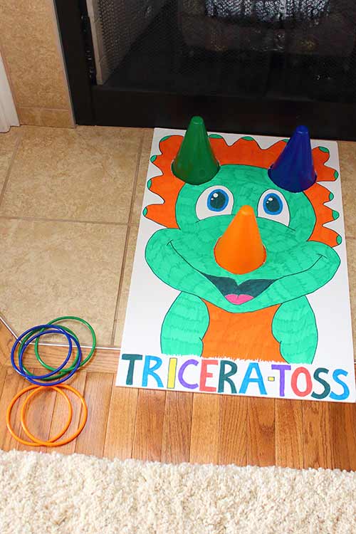a posterboard with a carton triceratops and cones sticking out of it where the horns should be, with rings for a game sitting next to it