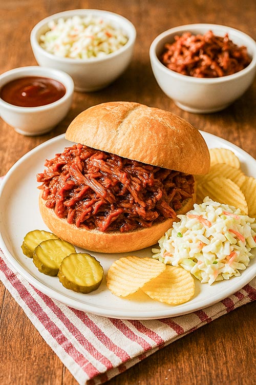 plate with a BBQ beef sandwich, pickles, chips, and colelsaw