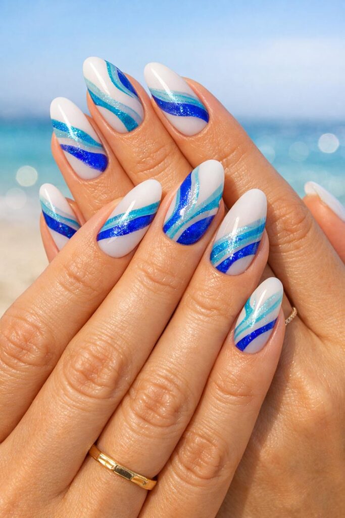 Almond nails with blue wave design and glitter on milky white base