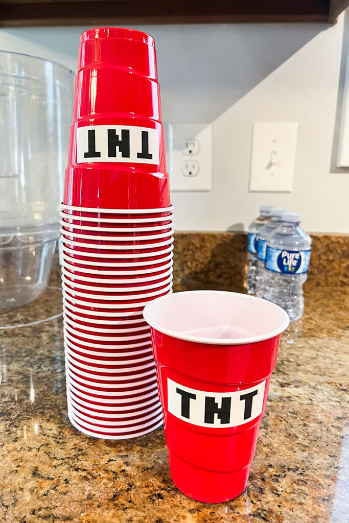 Red plastic party cups decorated with white labels spelling “TNT” in a Minecraft-style block font.