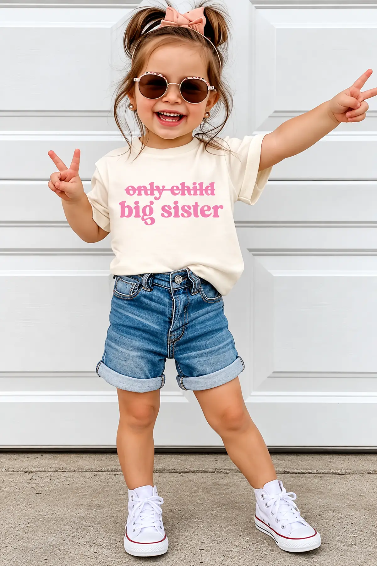 Smiling little girl wearing an "Only Child" crossed-out "Big Sister" shirt for a pregnancy announcement with a sibling.
