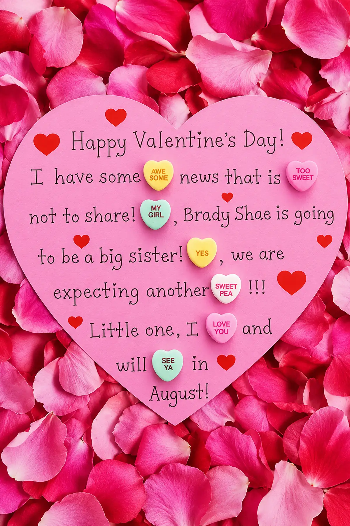 Pink Valentine's Day pregnancy announcement card surrounded by rose petals with conversation heart candies revealing a new baby.