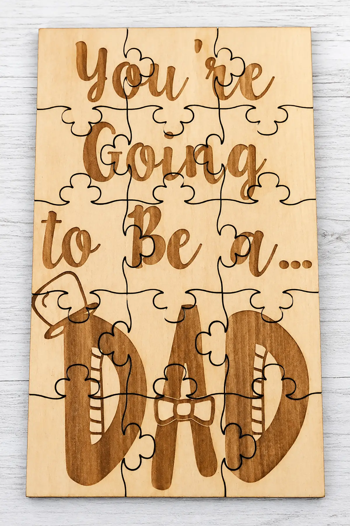 Wooden pregnancy announcement puzzle reading "You're Going to Be a Dad" with engraved lettering, displayed on a whitewashed wood background.