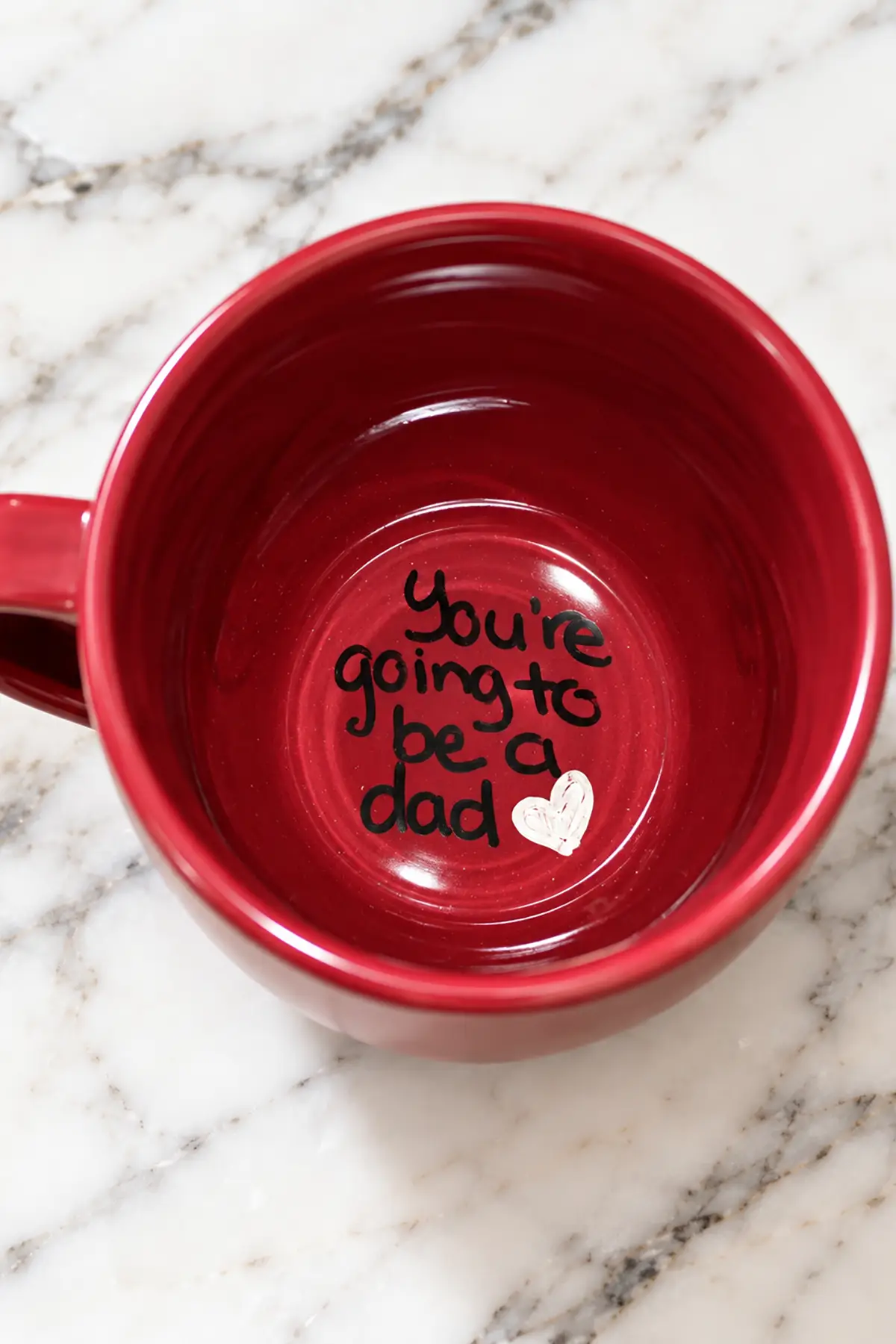 Red coffee mug with a handwritten "You're going to be a dad" message and white heart inside the bottom.