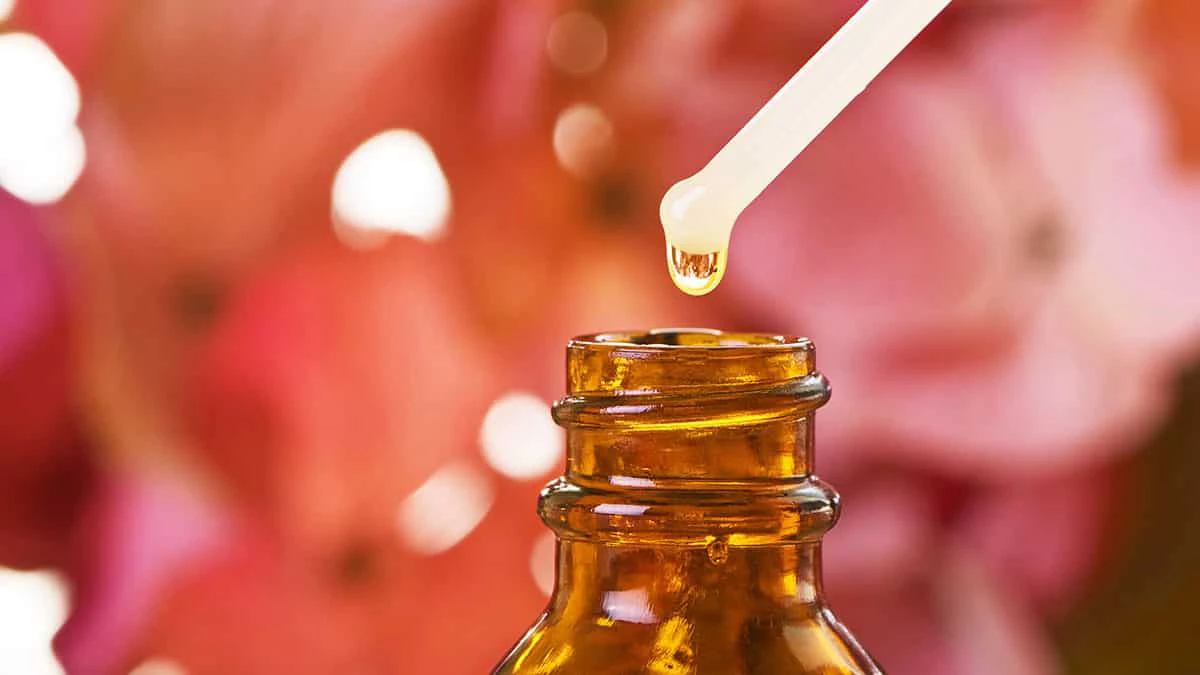 Close-up of a glass dropper releasing a golden liquid into an amber bottle, illustrating a homemade placenta tincture preparation.